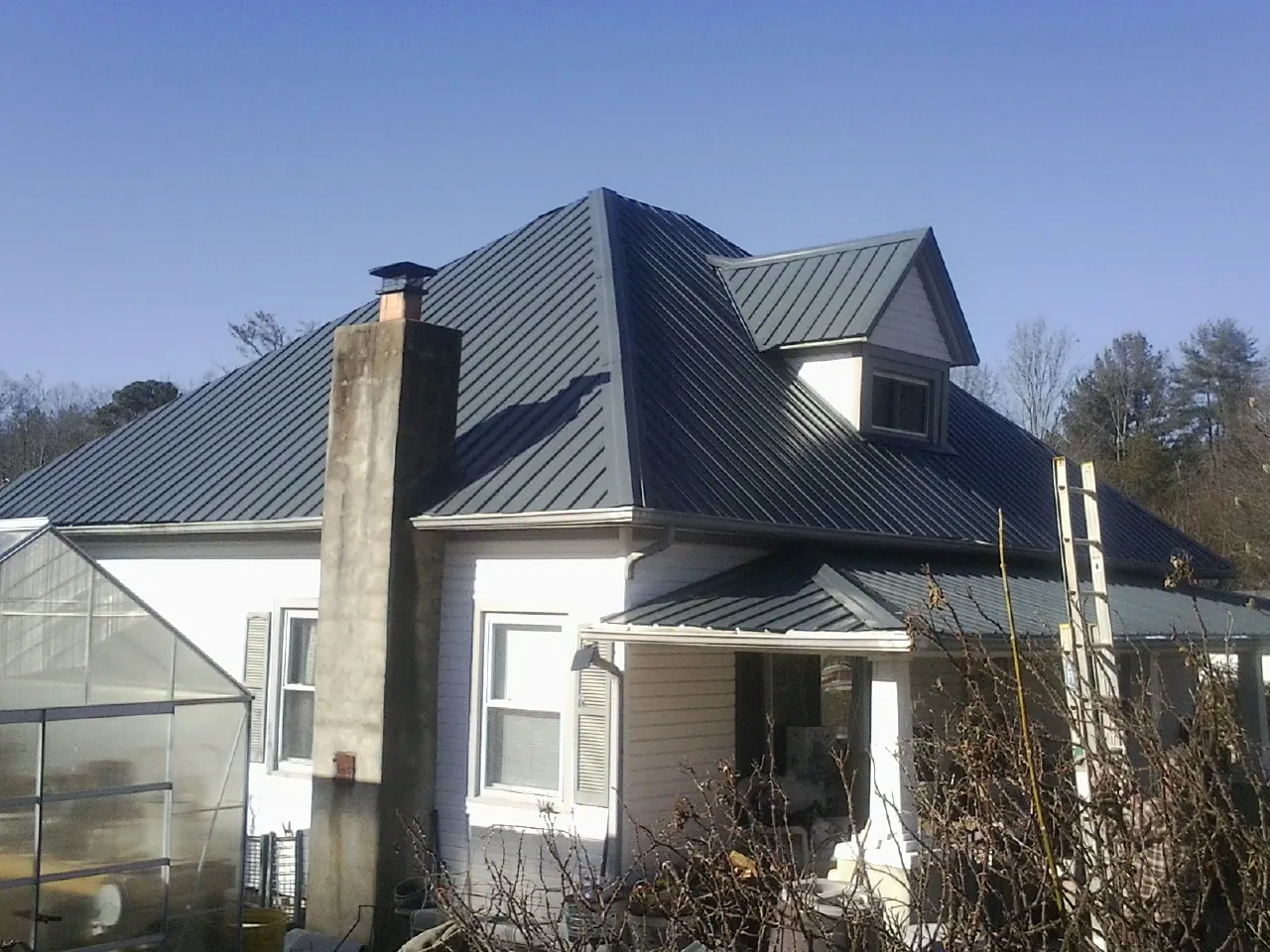 Dark blue standing seam metal roof on a white farmhouse with dormer — Slate & Tile Roof Repair by Roofing Brothers in Ashland City