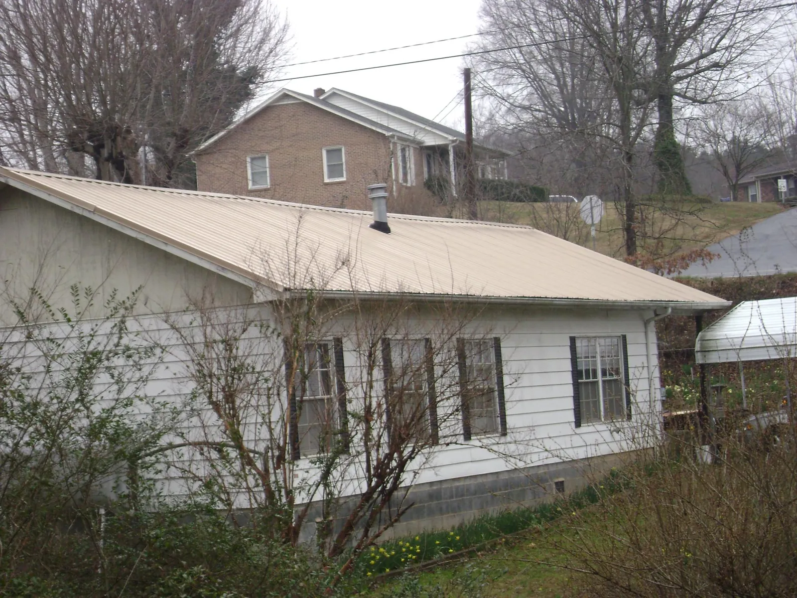 Tan metal roof on a white sided house set into a hillside — Commercial Roofing by Roofing Brothers in Ashland City